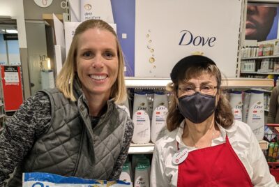 Two women stand beside a shelf filled with Dove products, showcasing a range of skincare and beauty items.
