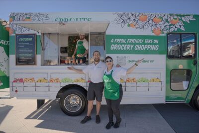 Two individuals standing near a green and white food truck, serving delectable treats.