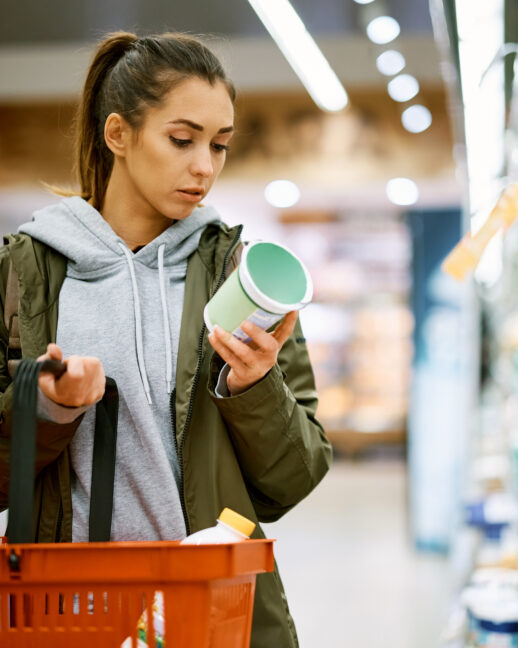 Young woman shopping in dairy aisle of grocery store; tariff uncertainty