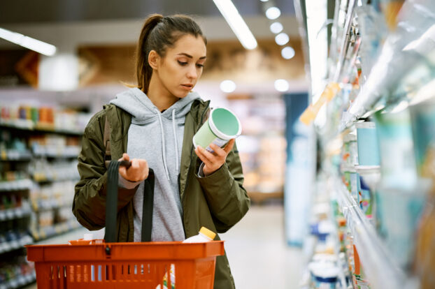 Young woman shopping in dairy aisle of grocery store; tariff uncertainty